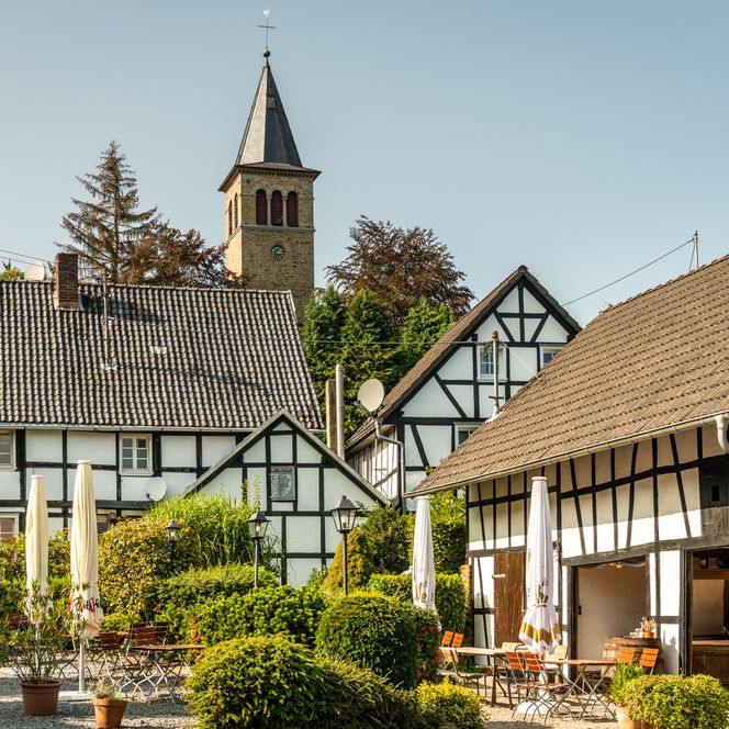 Fachwerkhäuser und Kirche mit Turm in idyllischem Dorf bei sonnigem Wetter.