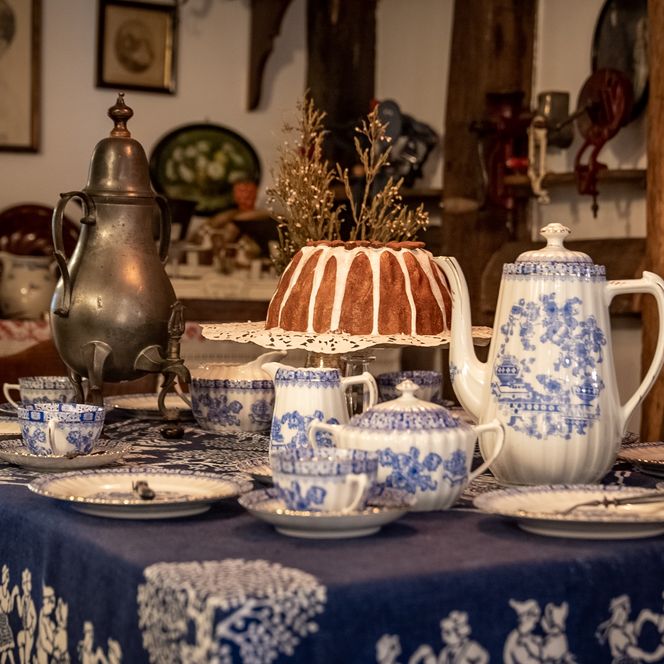 Ein gedeckter Tisch mit blau-weißem Porzellan, einer Kaffeekanne und einem Gugelhupf im Vintage-Stil.