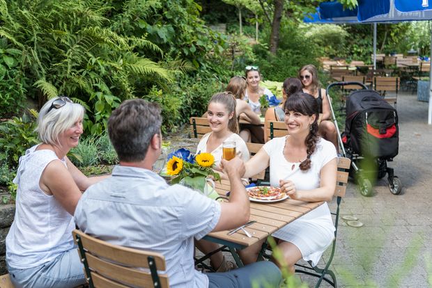 Vier Personen, drei Frauen und ein Mann, sitzen in einem Biergarten und trinken etwas