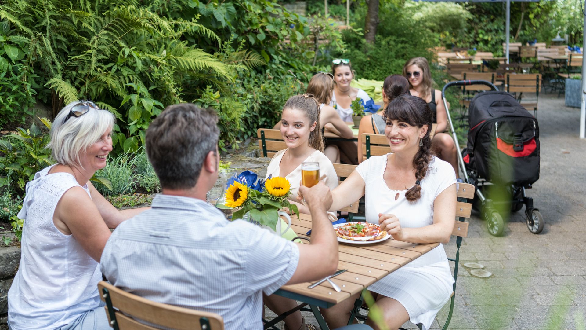 Vier Personen, drei Frauen und ein Mann, sitzen in einem Biergarten und trinken etwas