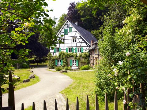 Blick über einen Zaun in die Natur, in der ein kleines Fachwerkhaus steht, zu dem ein Weg führt