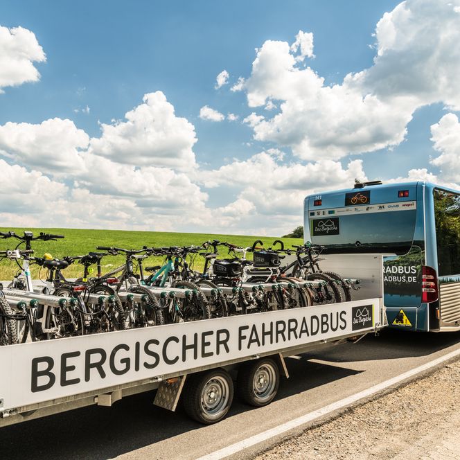 <p>Der Bergische Fahrradbus mit Fahrradanhänger auf einer Landstraße unter blauem Himmel.</p>