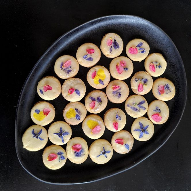 Selbstgebackene Kekse, mit Blüten dekoriert auf einem schwarzen Teller.