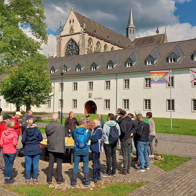 Eine Gruppe aus 15 Menschen steht in einem Halbkreis um ein Model. Im Hintergrund ist ein weißes Gebäude und der Altenberger Dom zu sehen.