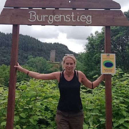 Foto der Gästeführerin Miriam Blümel, die in grüner Landschaft steht und sich mit beiden Händen an zwei Pfosten festhält.