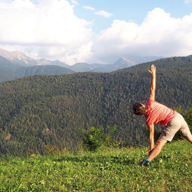 Eine Frau macht eine Yogaübung. Im Hintergrund ist weite, grüne Landschaft zu sehen.