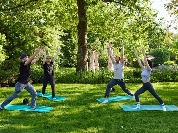 Vier Personen stehen in einem Park und machen Yoga-Übungen.