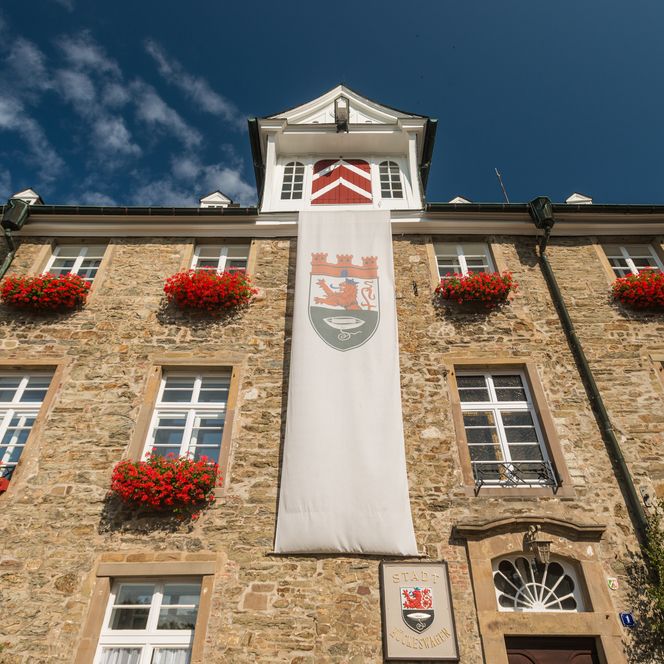 Historisches Rathaus Hückeswagen mit Fachwerkfassade, roten Geranien und klarem blauen Himmel.