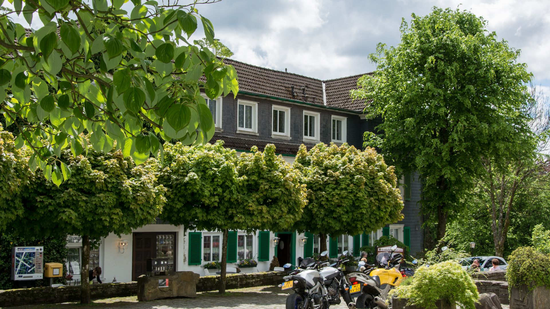 Restaurant mit Biergarten hinter einigen Bäumen auf einem Dorfplatz