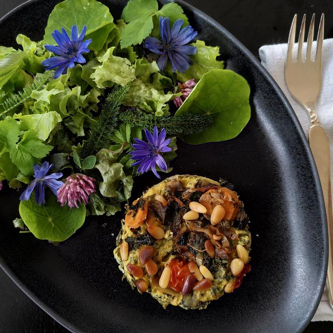 Ein Teller mit einem bunten Salat und vegetarischer Quiche, garniert mit essbaren Blüten.