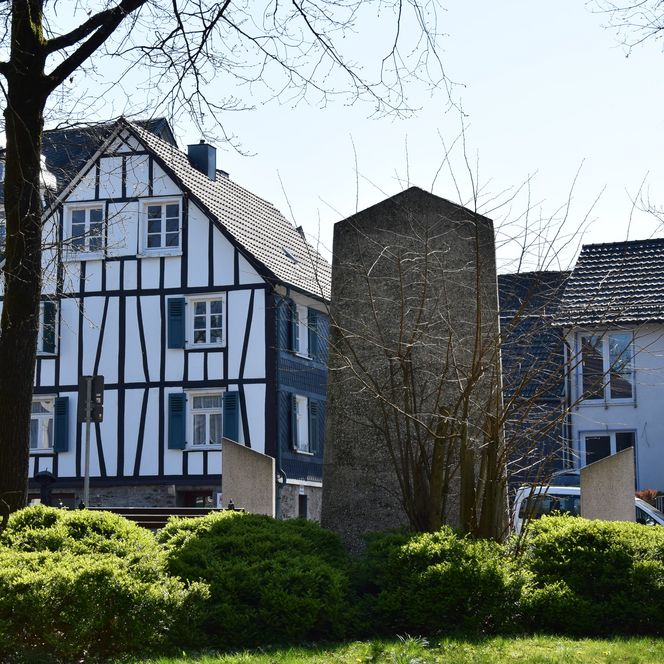 Das Bild zeigt idyllische Fachwerkhäuser und modernen Bau in einer grünen Umgebung eines Ortes.