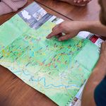 Karte auf Holztisch, mehrere Hände zeigen auf Wanderwege in einer grünen Landschaft in Burscheid.