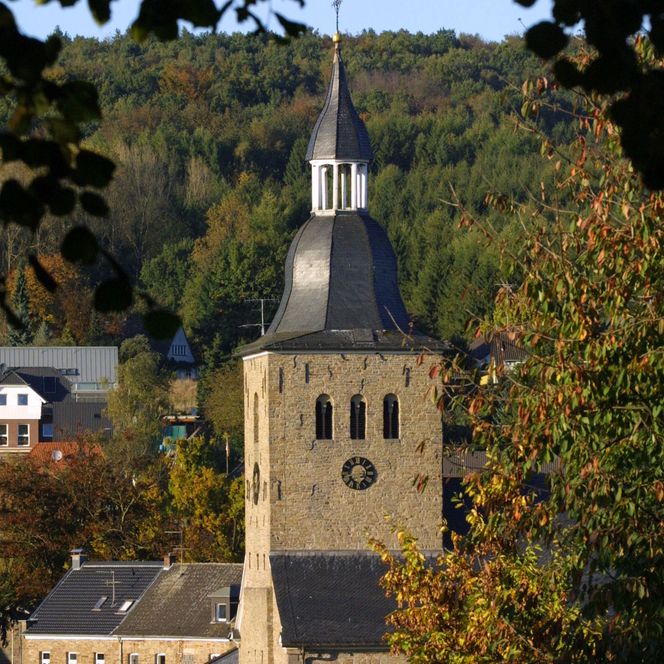 St. Severin Kirche in Lindlar, umgeben von Herbstlaub, mit einem markanten Turm vor bewaldeten Hügeln.