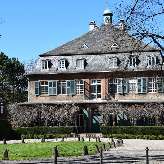 <p>Historisches Herrenhaus aus Backstein mit grünen Fensterläden, umgeben von gepflegtem Garten.</p>