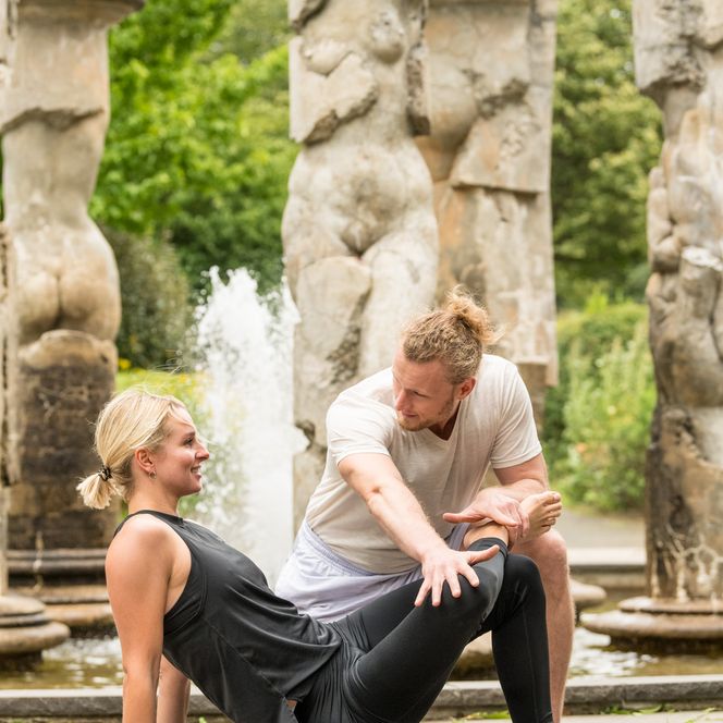 <p>Ein Paar beim Stretching vor antiken Säulen im Freien; sie verwenden eine Faszienrolle.</p>