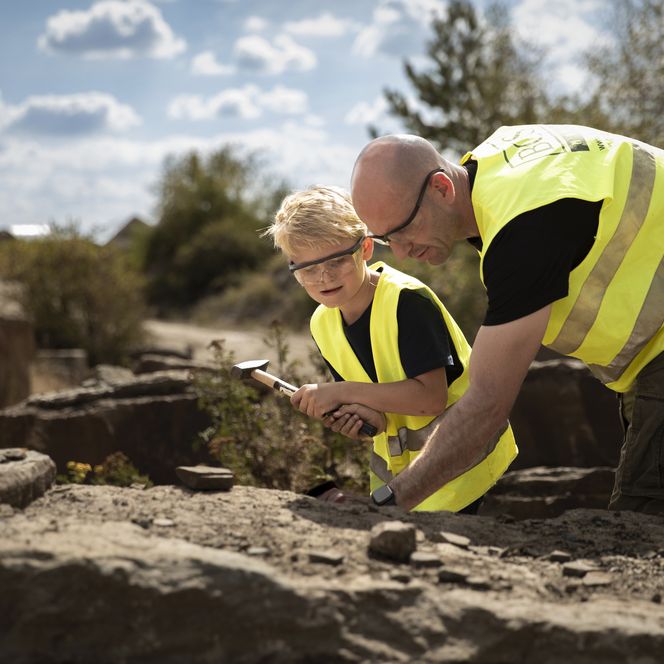 <p>Ein Erwachsener und ein Kind in gelben Westen erforschen gemeinsam Gesteine im Freien.</p>