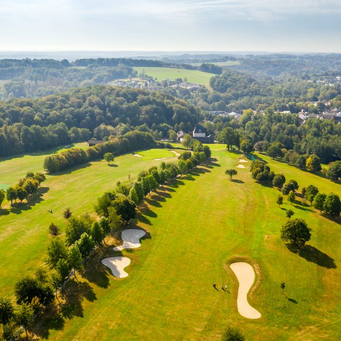 <p>Golfplatz in hügeliger Landschaft bei Much, umgeben von Bäumen und weiten, grünen Flächen.</p>