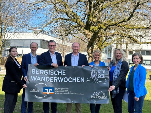 Sieben Menschen stehen in einem Halbkreis und halten gemeinsam ein Banner der Bergischen Wanderwoche in den Händen.