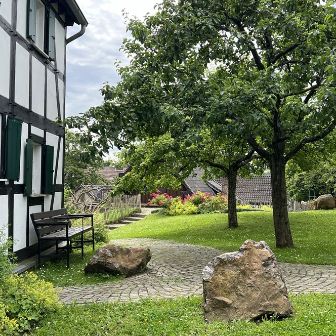 <p>Fachwerkhaus und blühender Garten mit Bäumen und Steinen in idyllischer Umgebung in Bergisch Gladbach.</p>