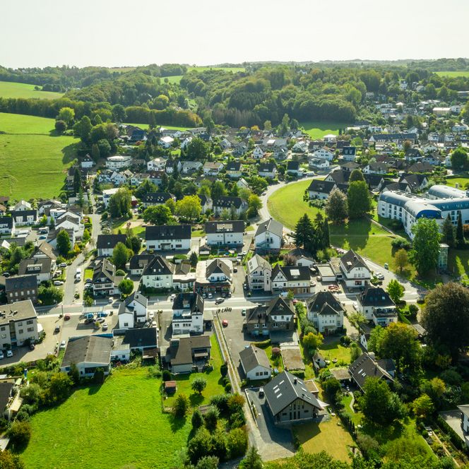 Luftaufnahme von Lohmar mit grünen Feldern, Wäldern und einer Siedlung aus Einfamilienhäusern.