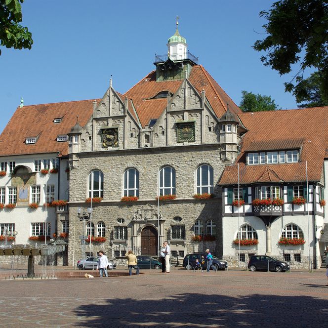 Historisches Rathaus mit roten Ziegeldächern und Blumendekoration auf einem sonnigen Marktplatz.