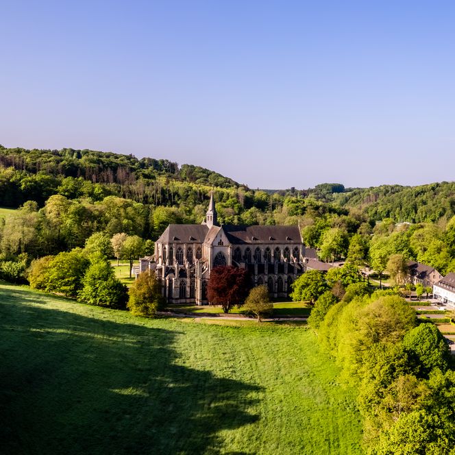 <p>Weitläufige Landschaft mit Abtei Altenberg im Grünen, umgeben von Hügeln und dichtem Wald.</p>