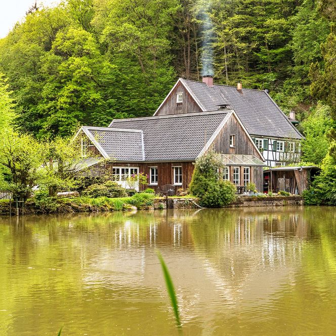 Fachwerkhaus am ruhigen Waldrand, idyllisch an einem kleinen See gelegen, mit rauchendem Kamin.