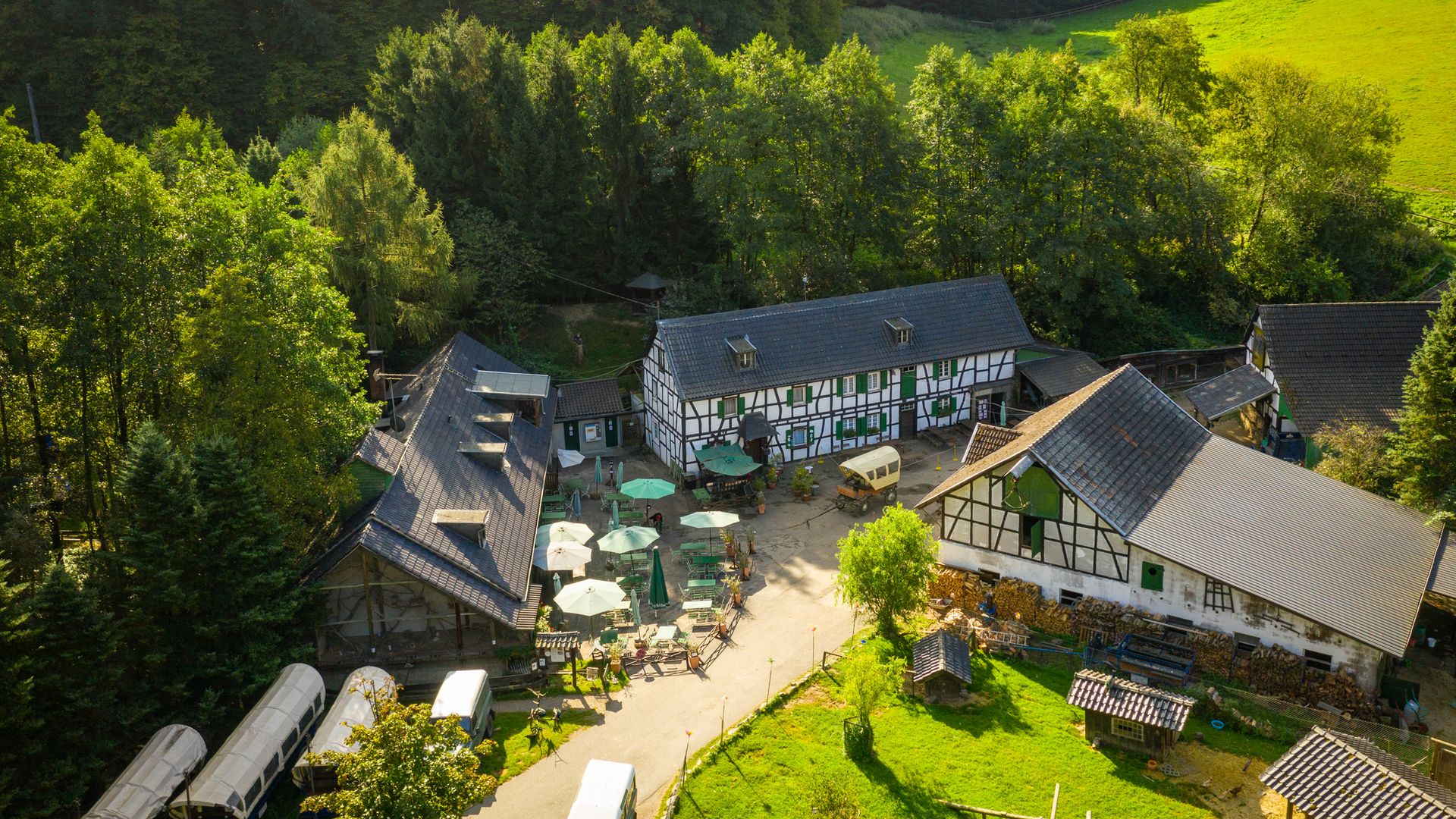 Blick von oben auf einen großen Hof mit Fachwerkhäusern, Planwagen und Restaurantbetrieb, die Gammersbacher Mühle.