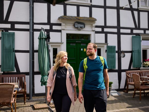 Ein Pärchen in Wanderkleidung spaziert vor einem Fachwerkhaus.