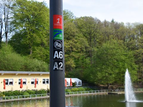 Markierungszeichen an einem Latenenpfahl vor einem Teich mit Wasserfontäne