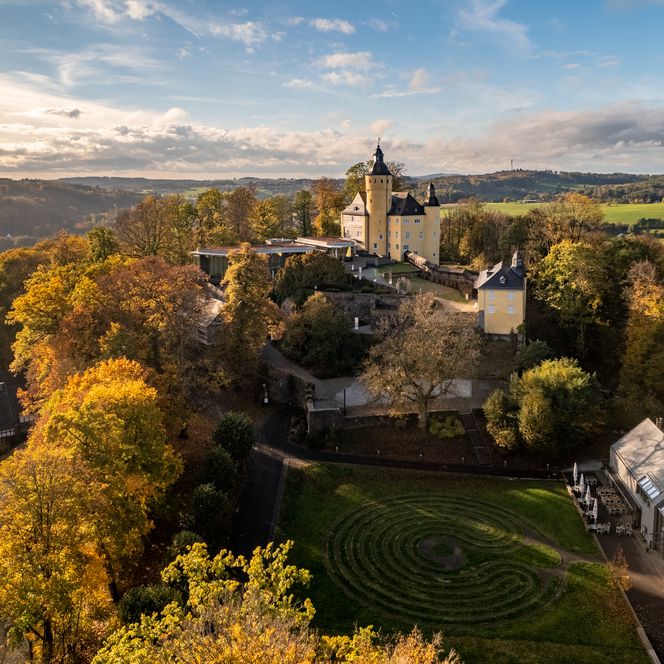 <p>Panorama der historischen Burg Nümbrecht umgeben von herbstlichem Wald und ländlicher Hügellandschaft.</p>