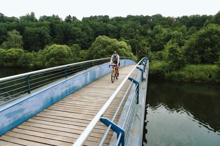 Ein Radfahrer fährt über eine Holzbrücke über einem Fluss. 