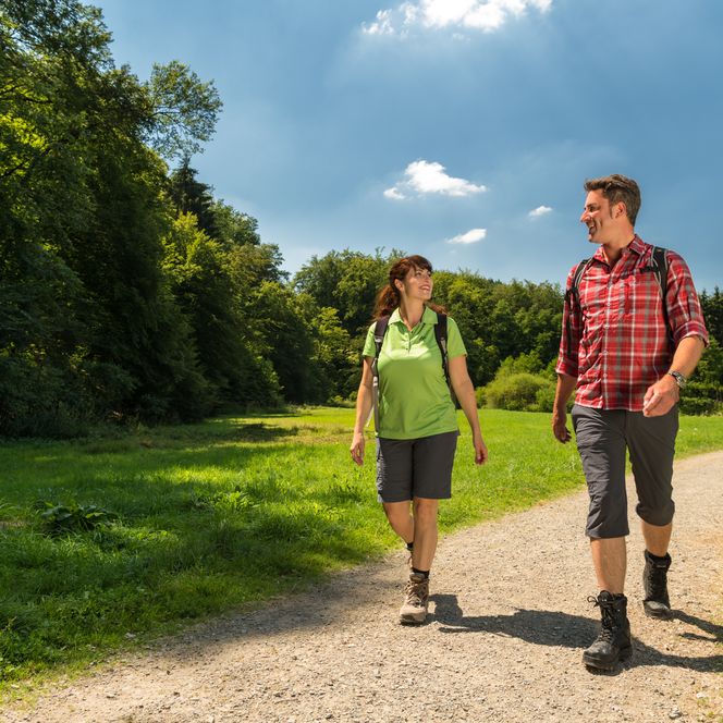 Wanderpaar genießt sonnigen Tag auf idyllischem, von Bäumen gesäumtem Wanderweg.