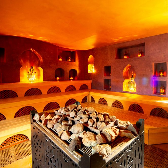 Sauna mit orientalischem Flair, kuscheligem Ambiente, warmem Licht und großen Steine im Zentrum.