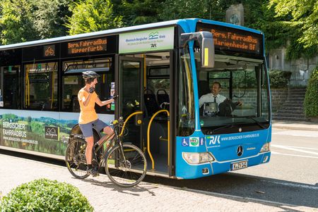 Ein Radfahrer spricht mit einem Busfahrer vor einem blauen Bergischen Fahrradbus.