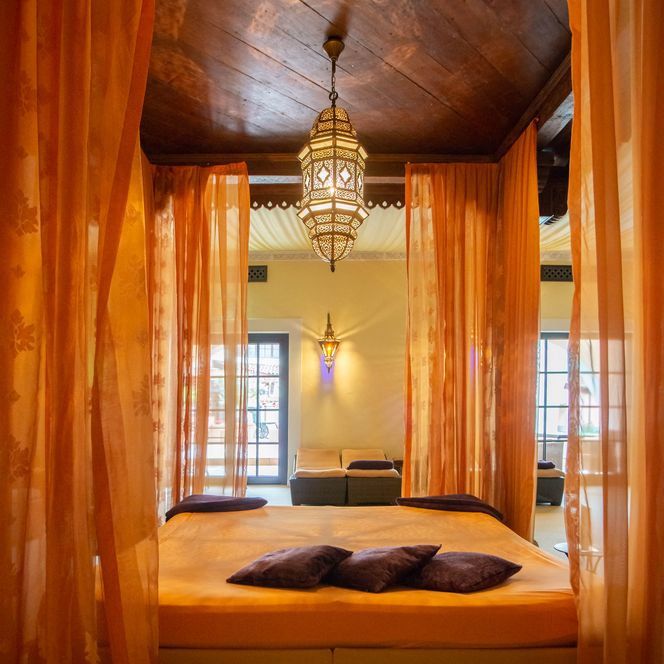 Ein luxuriöser, orientalisch inspirierter Raum mit Himmelbett und dekorativen Vorhängen.