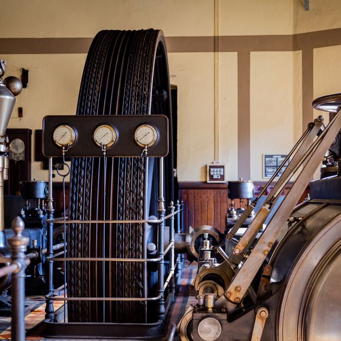 <p>Historische Maschinerie mit großen Zahnrädern und Druckanzeigen in einer alten Industrieräumlichkeit.</p>