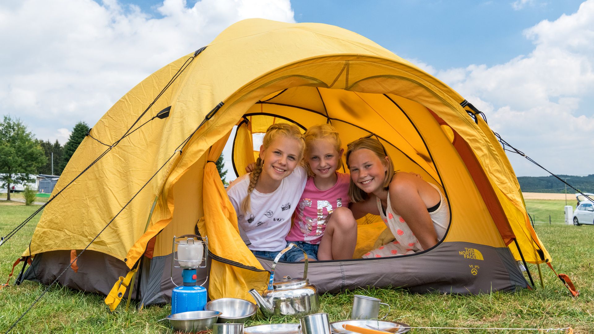 drei Kinder schauen aus einem gelben Kuppelzelt heraus