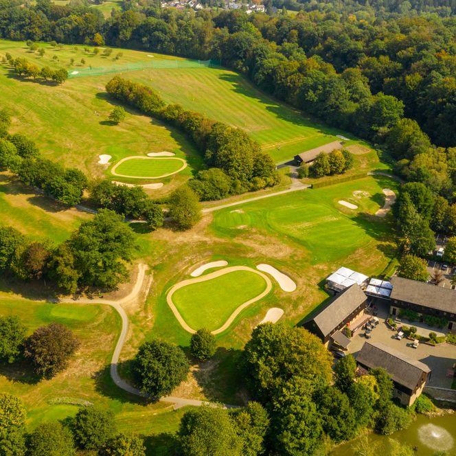 <p>Golfplatz Much in Hügellandschaft mit Clubhaus am Waldrand und Teich im Vordergrund, von oben gesehen.</p>