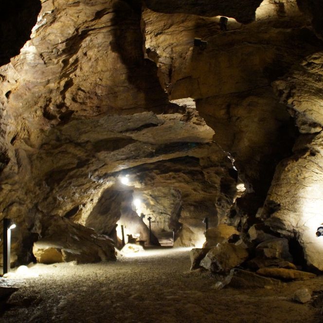 <p>Beleuchtete Tropfsteinhöhle mit sandigem Boden in Engelskirchen. Einzigartige Felsformationen.</p>