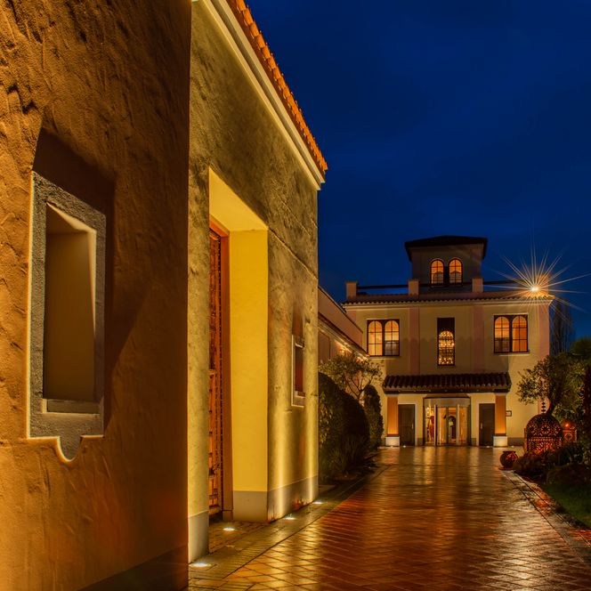Gelbes Gebäude im mediterranen Stil mit beleuchtetem Weg bei Dämmerung in Bergisch Gladbach.