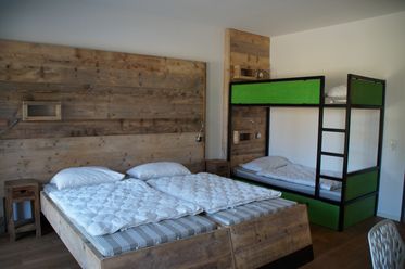Das Bild zeigt ein Zimmer mit Doppelbett und Etagenbett aus Holz, schlicht und gemütlich eingerichtet.