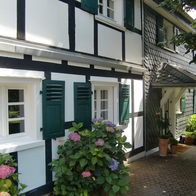 <p>Fachwerkhaus mit grünen Fensterläden und blühenden Hortensien in idyllischer Umgebung.</p>