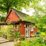 Kleines, rotes Gartenhaus umgeben von üppigem Grün und bunten Blumen im Dorf Much.