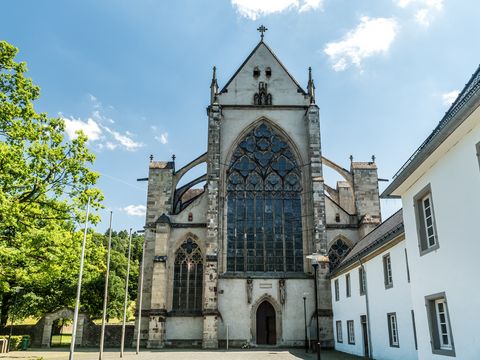 Ansicht Haupteingang Altenberger Dom bei schönem Wetter. Links stehen Bäume, rechts ist ein weiteres Gebäude.