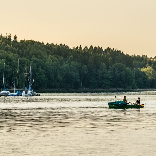Ein ruhiger See bei Hückeswagen mit Segelbooten am Ufer und zwei Personen in einem Ruderboot.