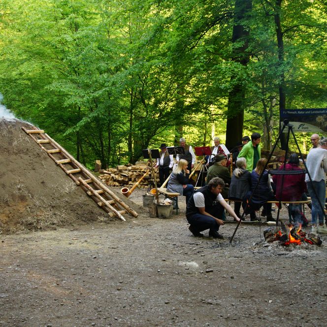 Wandergruppe steht im Wald neben einem rauchenden Meiler.