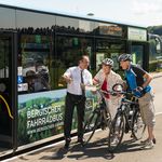 Busfahrer gibt Radfahrerpaar vor dem "Bergischen Fahrradbus" Auskunft. Fahrräder am Bus angelehnt.
