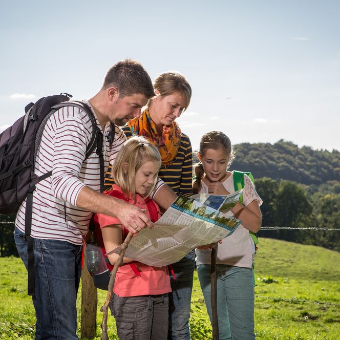 ```html <p>Familie mit Karte blickt in grüner Landschaft; Hügel im Hintergrund.</p> ```