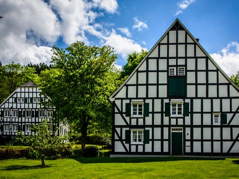 Ein großes und ein kleines Fachwerkhaus stehen auf einer Wiese zwischen Bäumen